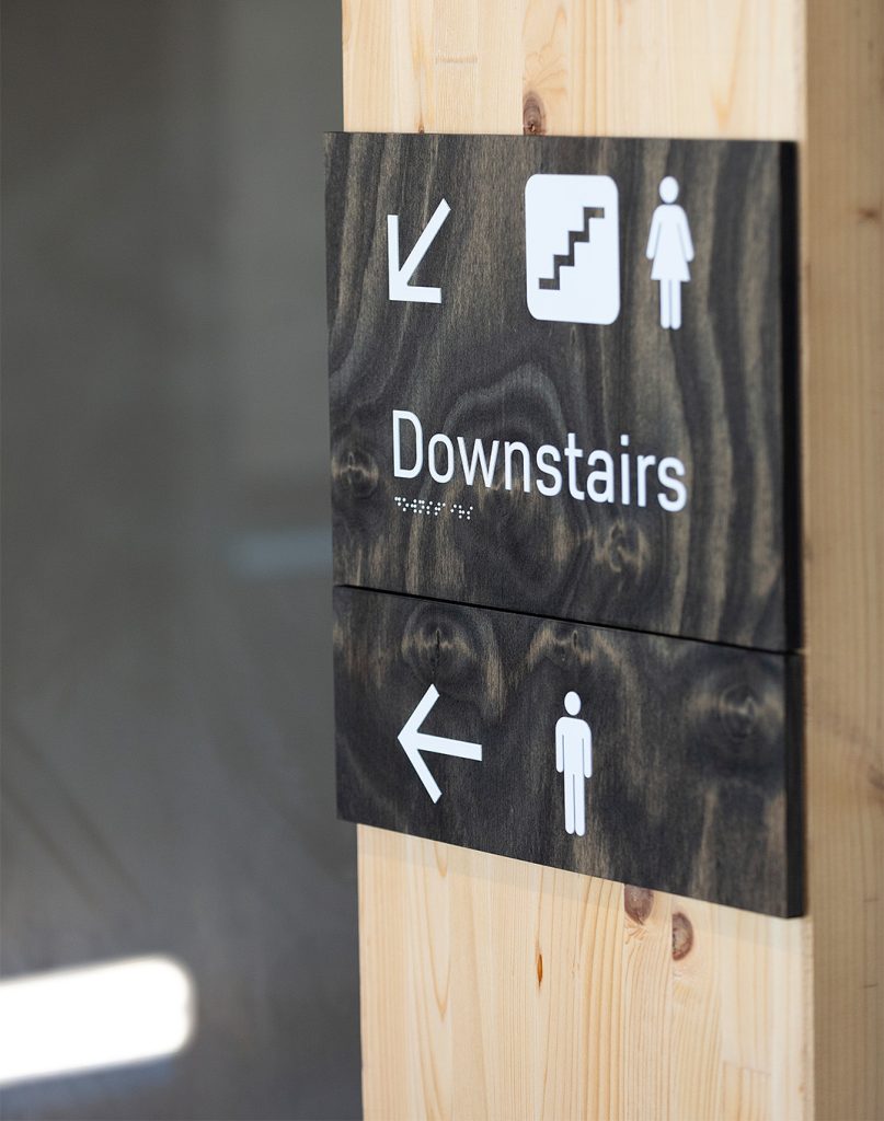 Braille and tactile wooden directional signage with universal pictograms.